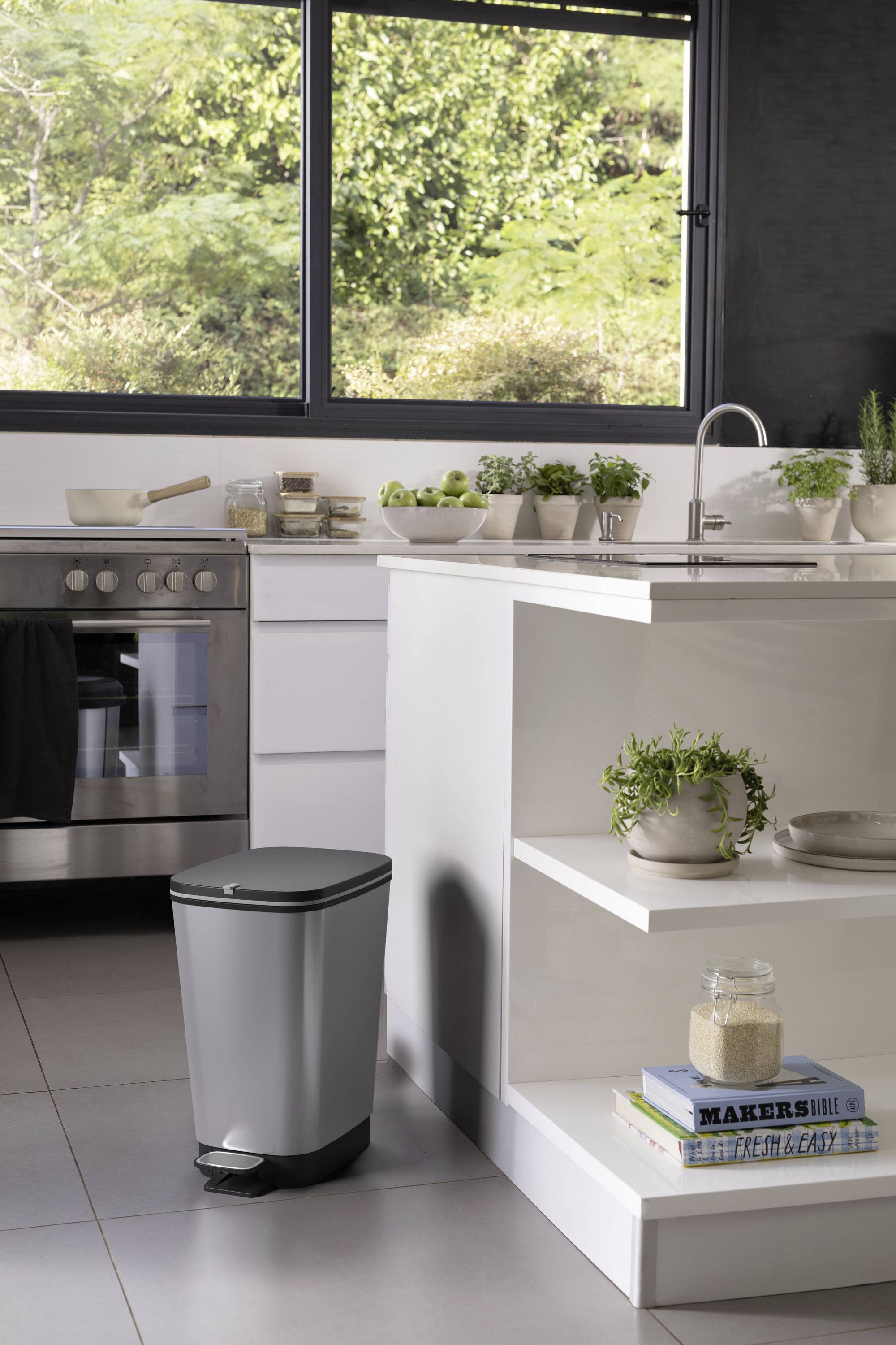 Küche mit modernem Design: weißes Interieur, Edelstahlgeräte, Pflanzen auf der Arbeitsfläche. Ein Mülleimer steht neben der Anrichte.