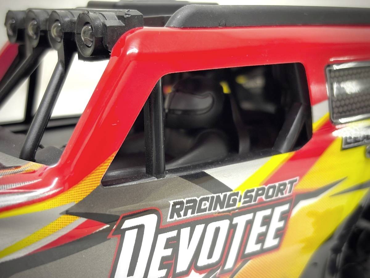 Ein Spielzeugauto mit rotem und grauem Design und der Aufschrift 'Racing Sport Devotee' auf der Seite. Es hat ein stabiles Überrollbügel.