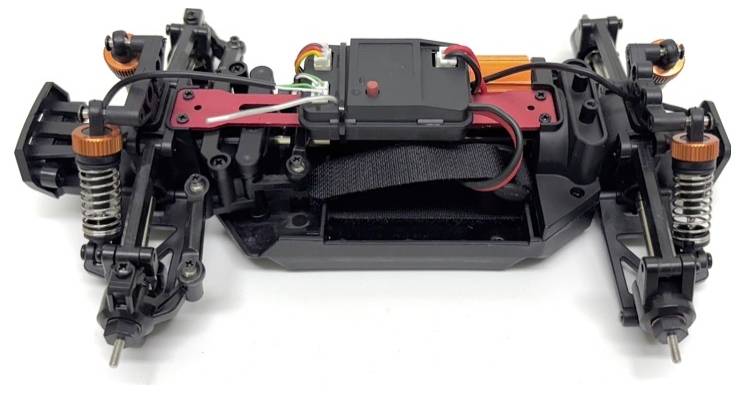 Ein ferngesteuertes Auto-Chassis mit sichtbarer Elektronik, Stoßdämpfern und Rädern. Kabel sind zur Steuerung angeschlossen.