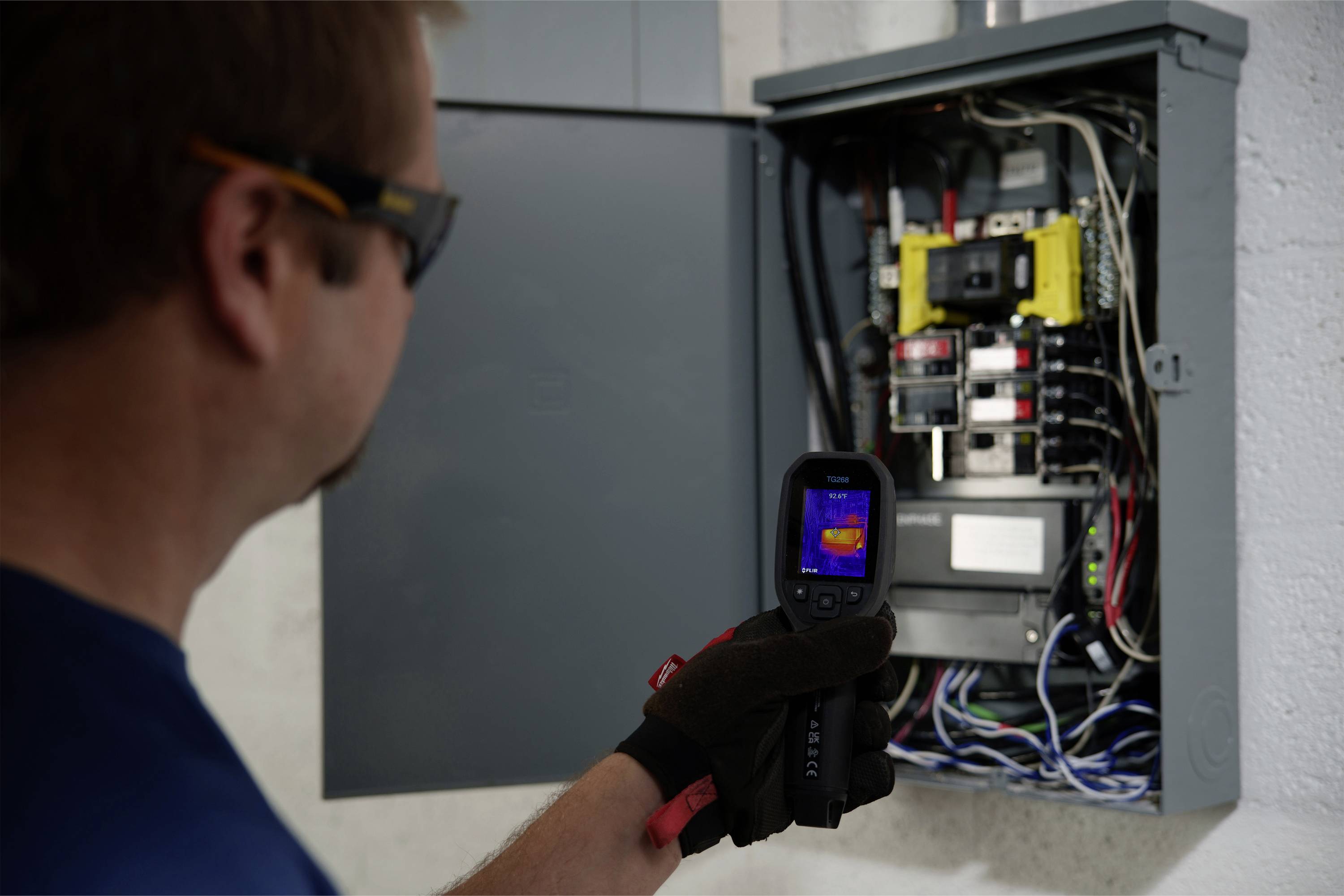 Eine Person verwendet eine Wärmebildkamera, um einen geöffneten elektrischen Schaltschrank zu untersuchen.