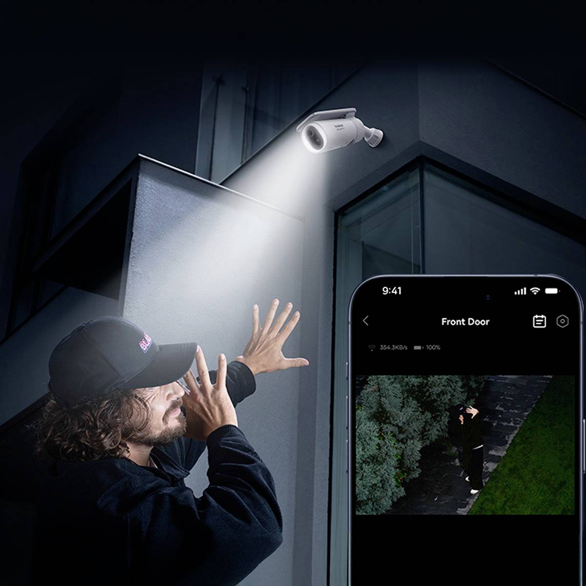 Ein Mann zeigt auf eine Überwachungskamera, die ein Bild auf ein Smartphone überträgt. Die Aufnahme zeigt eine Person vor einer Haustür.