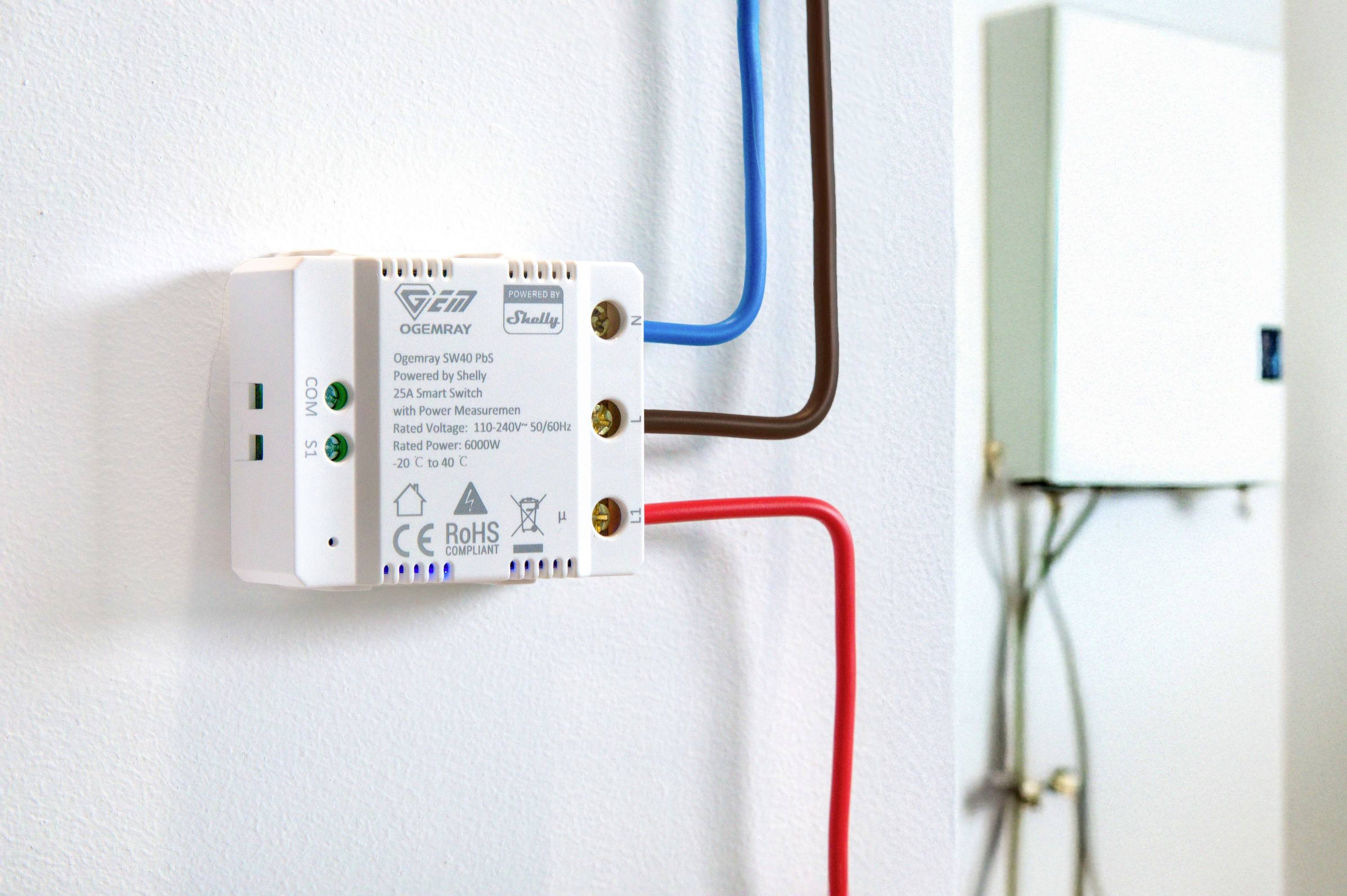 Ein Shelly-Modul zur smarten Lichtsteuerung, an einer Wand montiert. Kabel führen in eine Hauptstrombox.