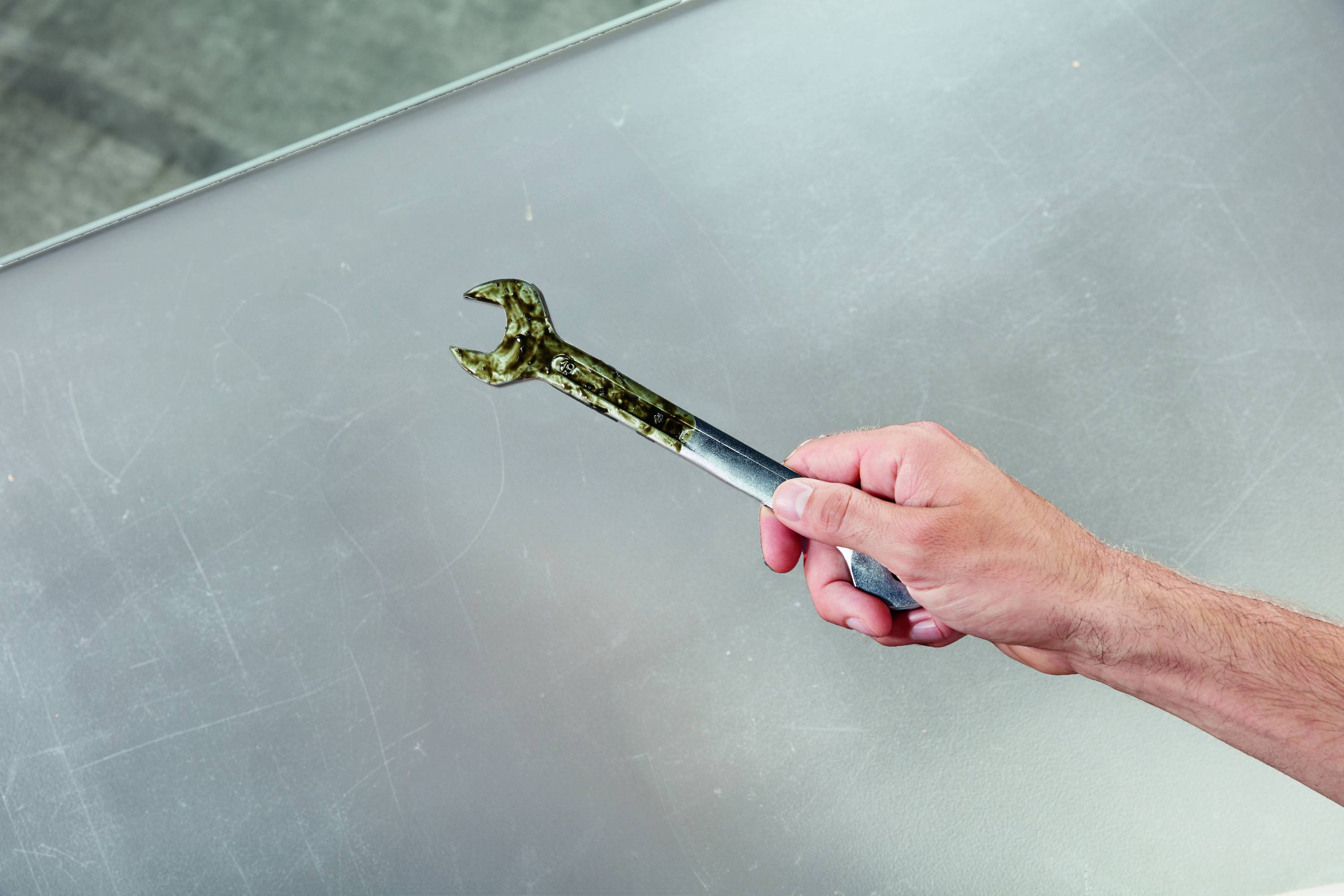 Eine Hand hält einen Schraubenschlüssel über einer grauen Oberfläche.