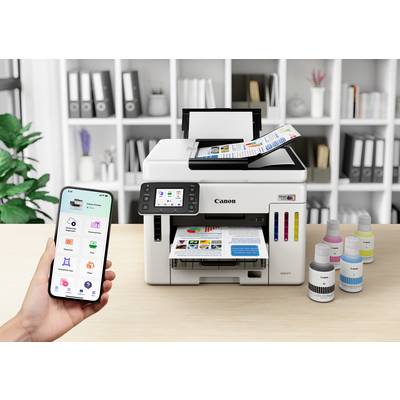 Eine Person bedient einen Drucker per Smartphone. Der Drucker auf einem Tisch druckt farbige Dokumente. Rechts daneben stehen Tintenflaschen.