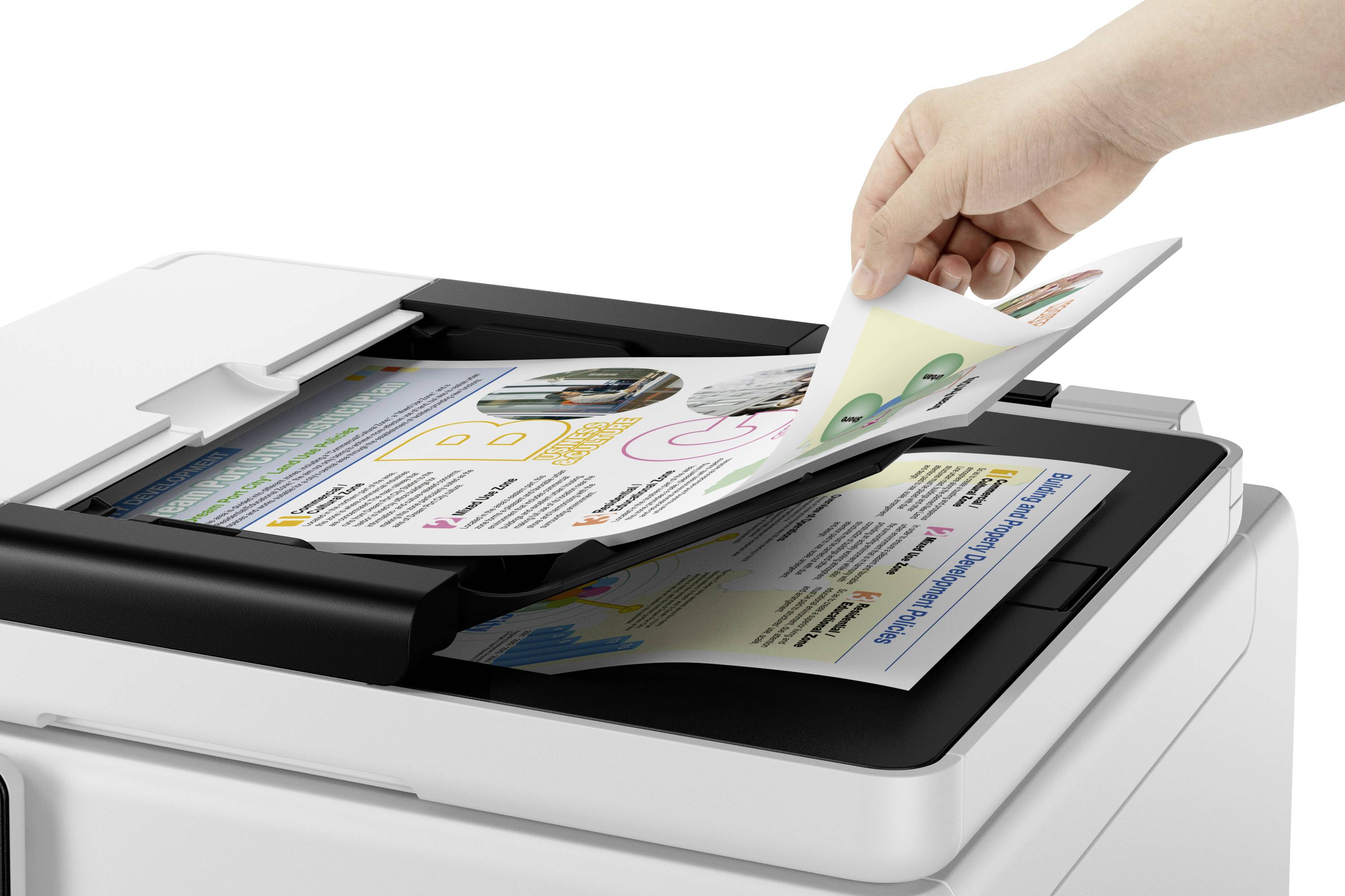 Hand legt ein Blatt Papier in einen Scanner oder Kopierer ein, auf dem bereits bunte Dokumente liegen.