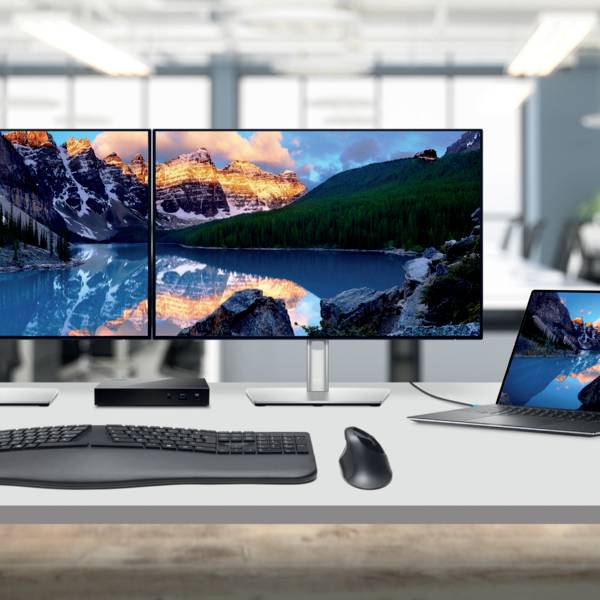 Zwei Monitore auf einem Tisch zeigen eine Landschaft mit Bergen und See. Daneben ein Laptop mit ähnlichem Hintergrundbild. Im Büro.