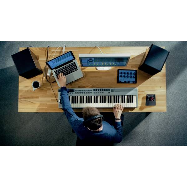Eine Person sitzt an einem Schreibtisch, arbeitet mit einem Laptop und einem Keyboard. Über Kopfhörer hört sie möglicherweise Musik.