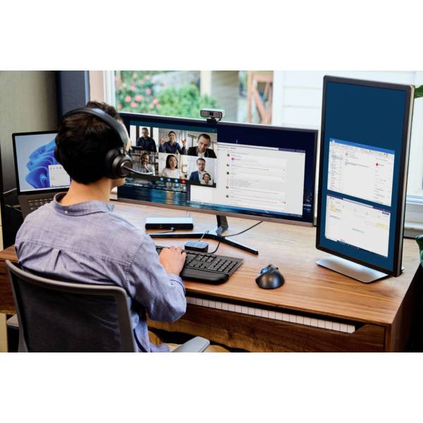 Eine Person arbeitet an einem Schreibtisch mit mehreren Bildschirmen, auf denen Videoanrufe und Software-Anwendungen sichtbar sind.