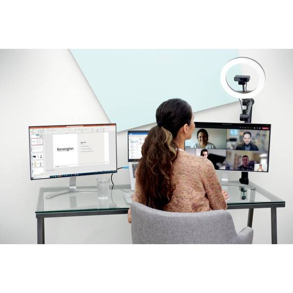 Eine Frau sitzt an einem Schreibtisch vor zwei Computermonitoren, nimmt an einer Videokonferenz mit mehreren Teilnehmern teil.