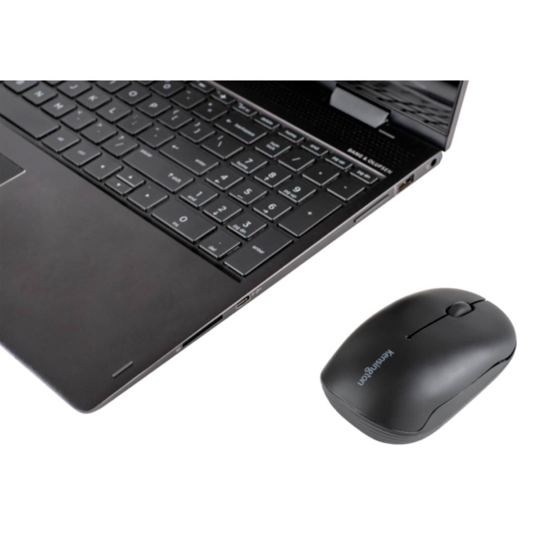 Ein Laptop mit geöffneter Tastatur, daneben eine schwarze kabellose Computermaus auf einer weißen Oberfläche.