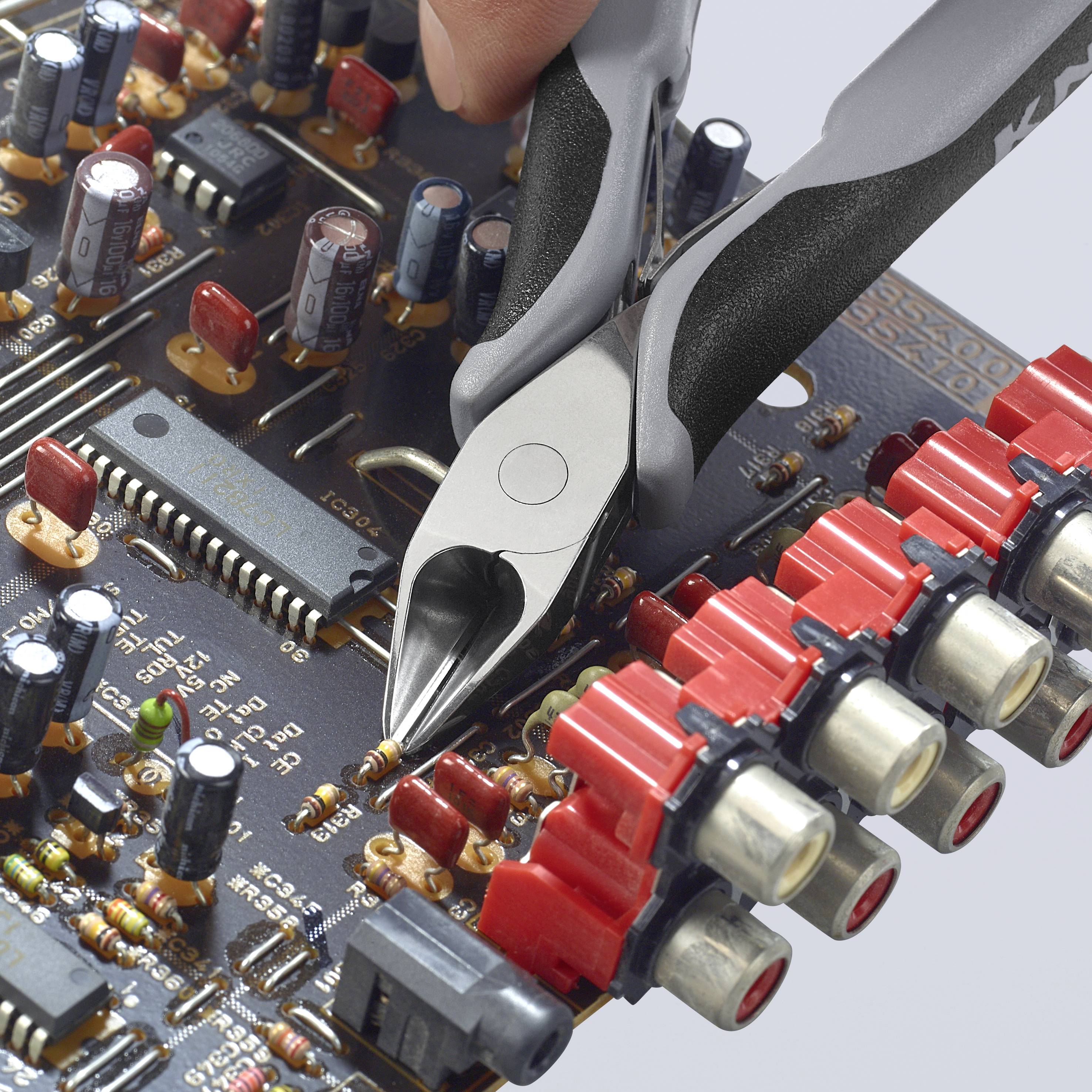Eine Hand hält Zangen und schneidet Drähte auf einer Leiterplatte. Umgeben von elektronischen Bauteilen und Steckverbindungen.
