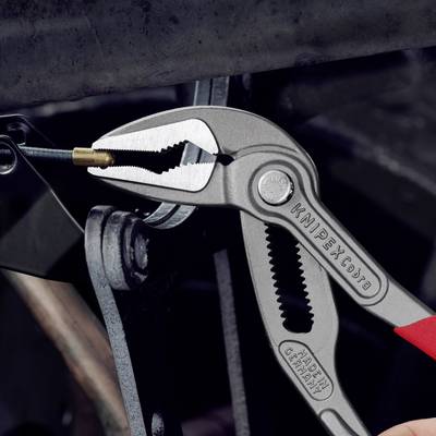 Eine Hand hält eine silberne Zange mit rotem Griff, die eine kleine Schraube festhält. Die Zange hat die Aufschrift 'KNIPEX'.