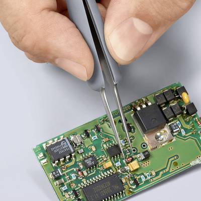 Eine Hand hält eine Pinzette und platziert ein kleines elektronisches Bauteil auf einer grünen Leiterplatte, die diverse Schaltkreise zeigt.