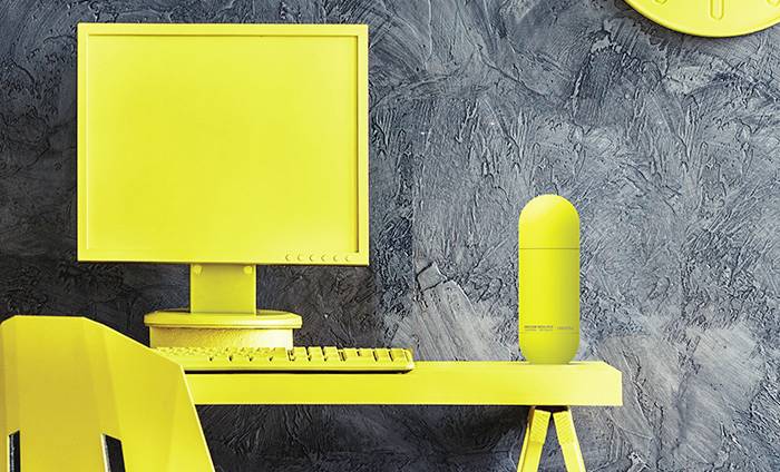 Gelber Arbeitsplatz mit Computer, Tastatur und Flasche auf Schreibtisch vor einer grauen Wand. Moderner, monochromatischer Stil.