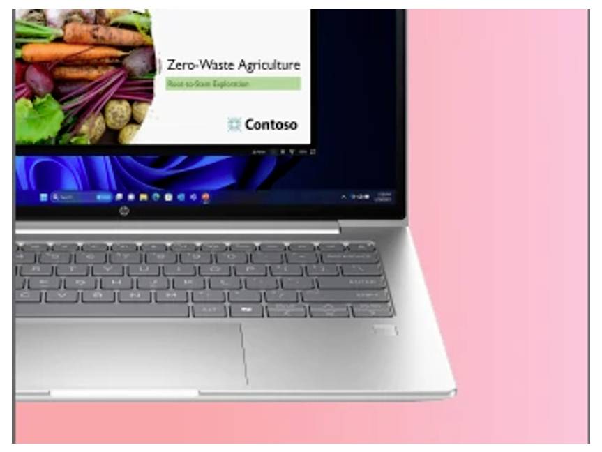 Ein Laptop auf einem pinken Hintergrund zeigt eine Präsentation mit dem Titel „Zero-Waste Landwirtschaft", die ein Bild von Gemüse und das Contoso-Logo enthält.