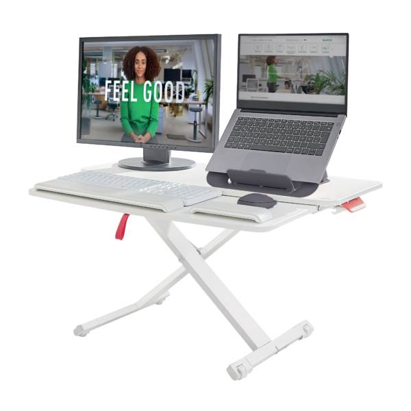 'Feel Good' wird auf einem Computerbildschirm hinter einem Laptop angezeigt. Beide Geräte sind auf einem höhenverstellbaren Tisch platziert.