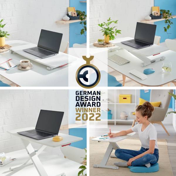 Ein Laptop steht auf einem höhenverstellbaren Laptopständer auf einem Tisch. Im Hintergrund sitzt eine Frau auf dem Boden und schreibt in ein Notizbuch. Der Ständer ist mit dem Label 'German Design Award Winner 2022' ausgezeichnet.