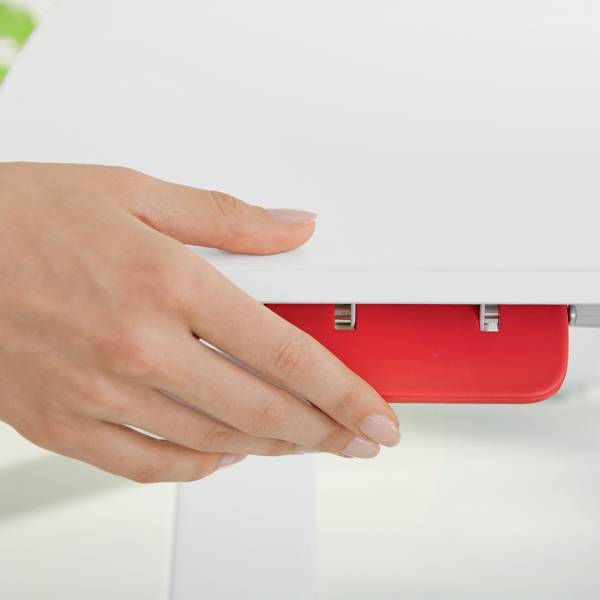 Eine Hand nutzt einen roten Locher auf einem weißen Tisch. Der Locher stanzt ein Blatt Papier.