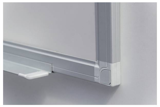 Eine Ecke eines silbernen Whiteboards mit halterung für Stifte an der linken Seite. Hintergrund ist eine weiße Wand.