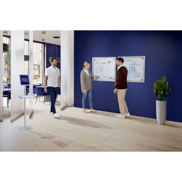 Drei Personen interagieren in einem modernen Büro vor einer großen Tafel an der Wand. Die Tafel zeigt Diagramme und Informationen.