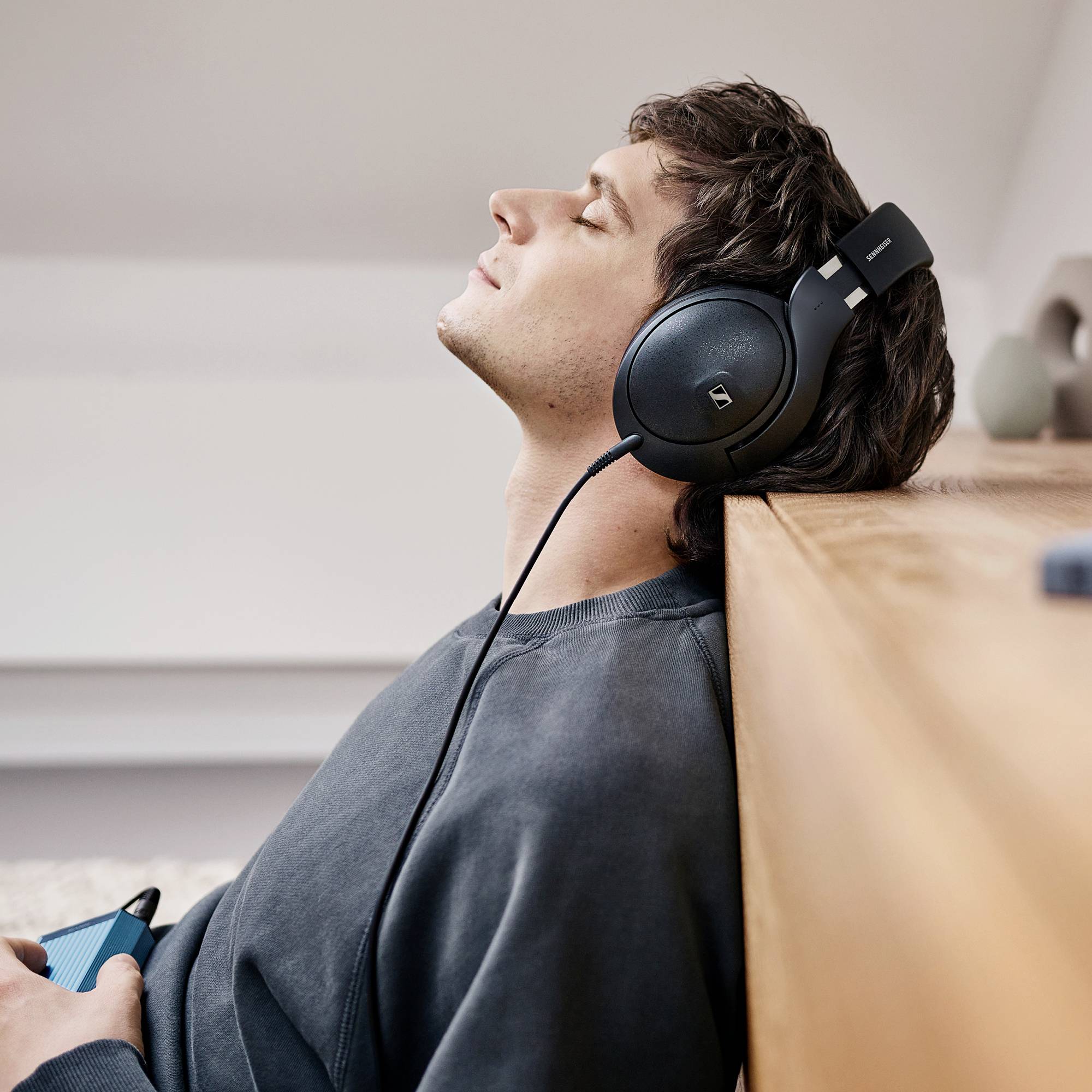 Eine Person liegt entspannt auf einem Sofa und trägt große Kopfhörer. Sie scheint Musik zu hören oder sich zu entspannen.