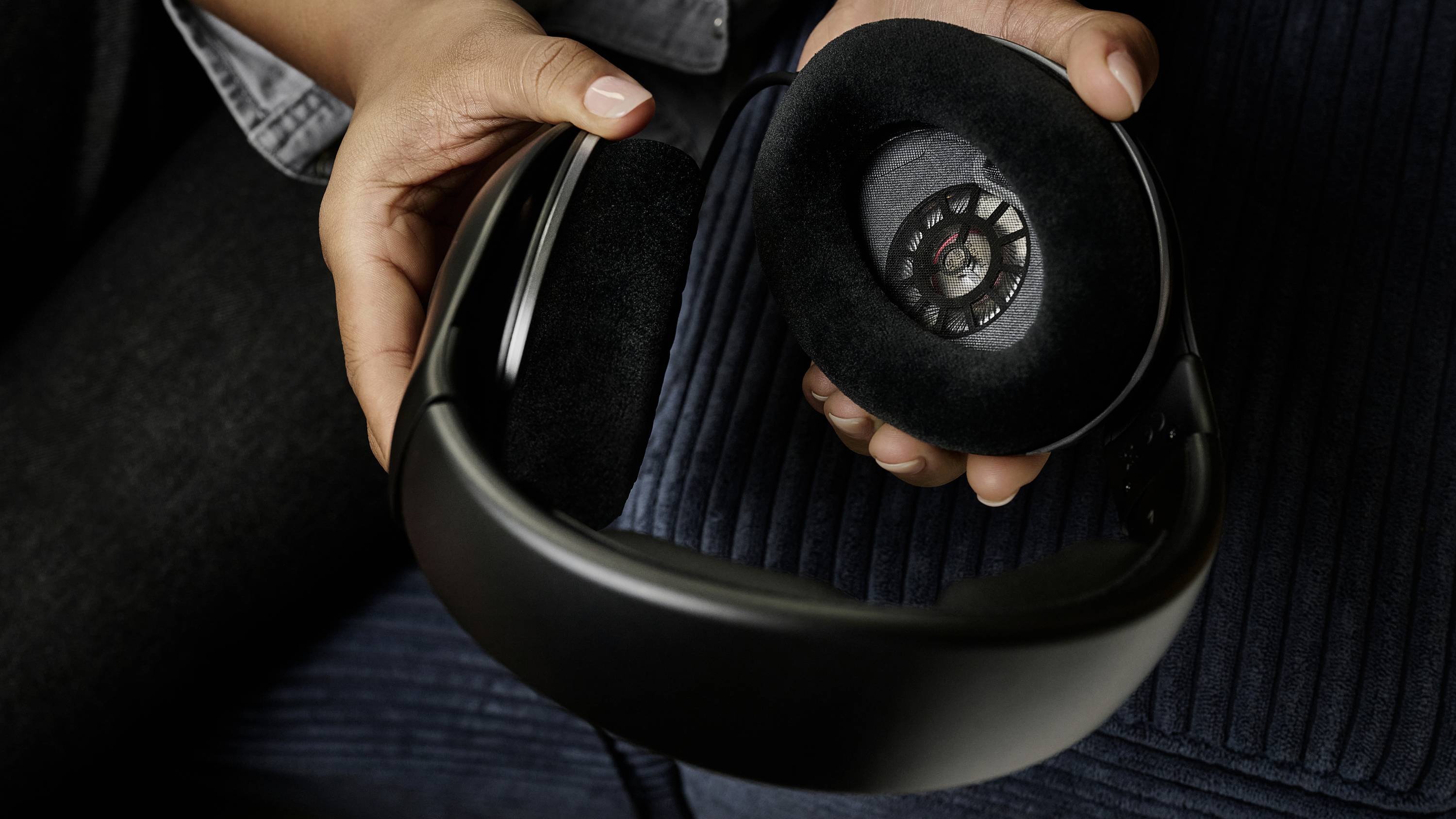 Eine Person hält einen schwarzen Kopfhörer mit einem abgenommenen Ohrpolster in der Hand.