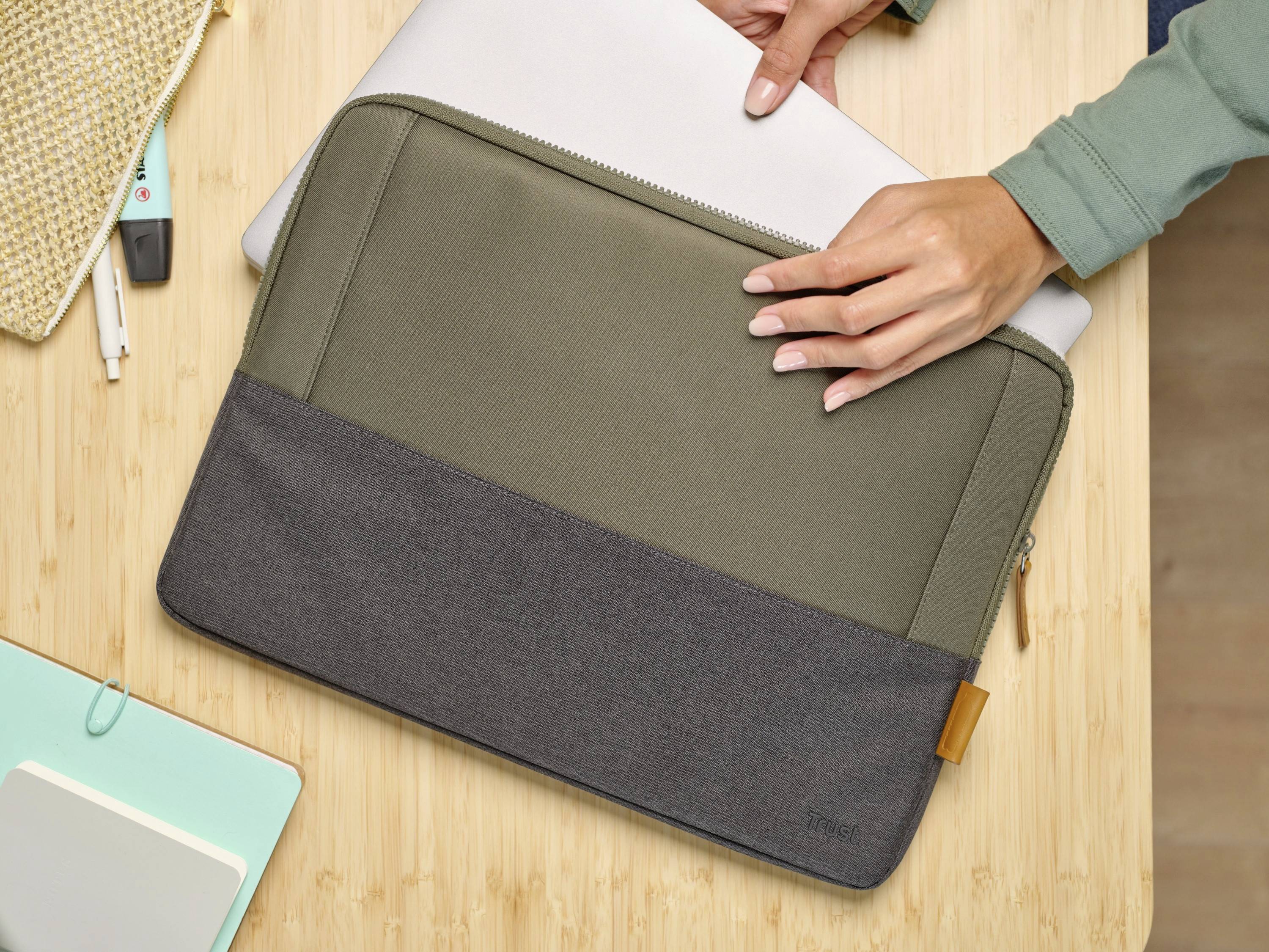 Person legt einen Laptop in eine zweifarbige Laptop-Hülle. Hülle liegt auf einem Holztisch.