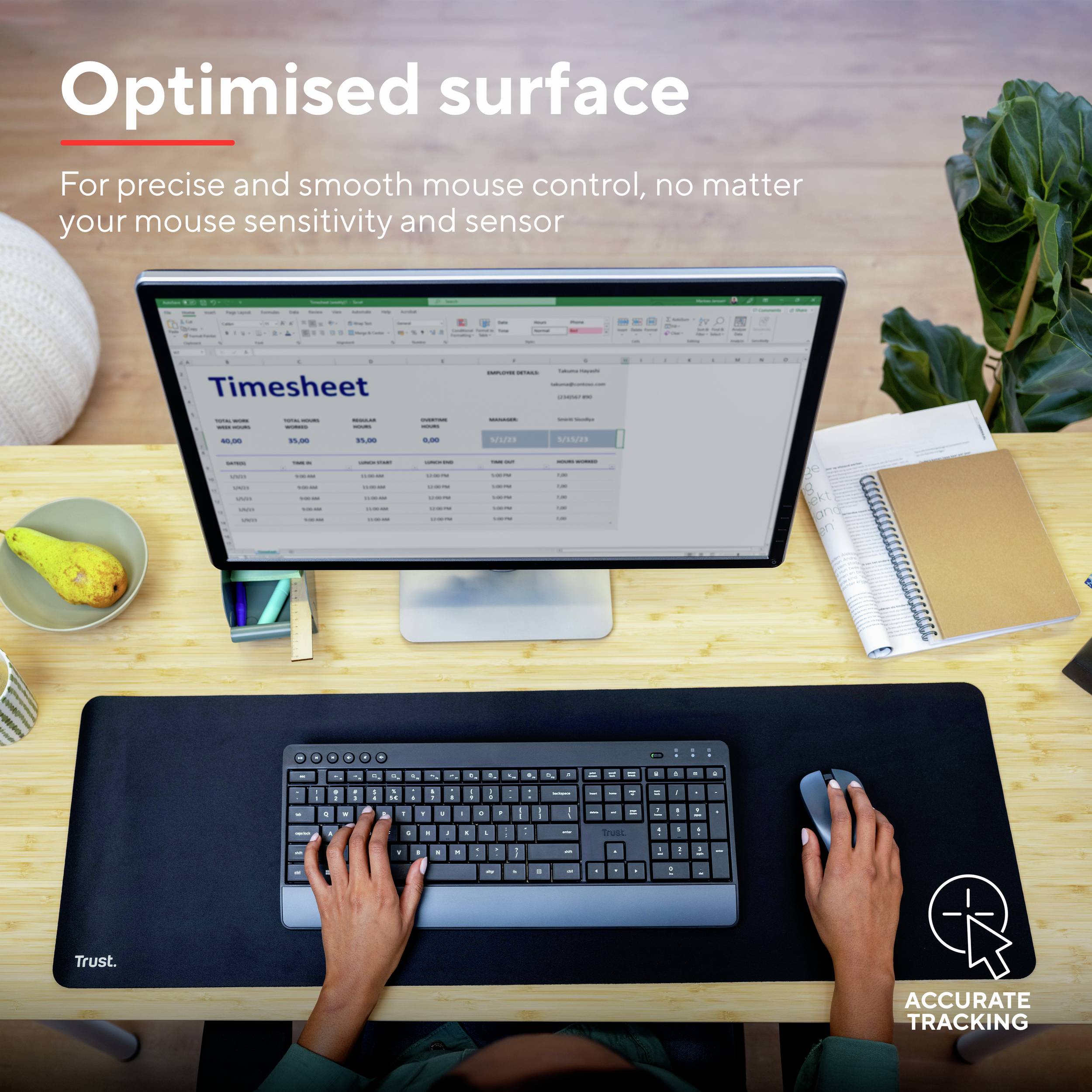 Ein Computermonitor mit einer geöffneten Zeiterfassungstabelle. Hände auf einer Tastatur auf einer glatten, schwarzen Mausmatte. Im Hintergrund Pflanzen und Schreibutensilien.