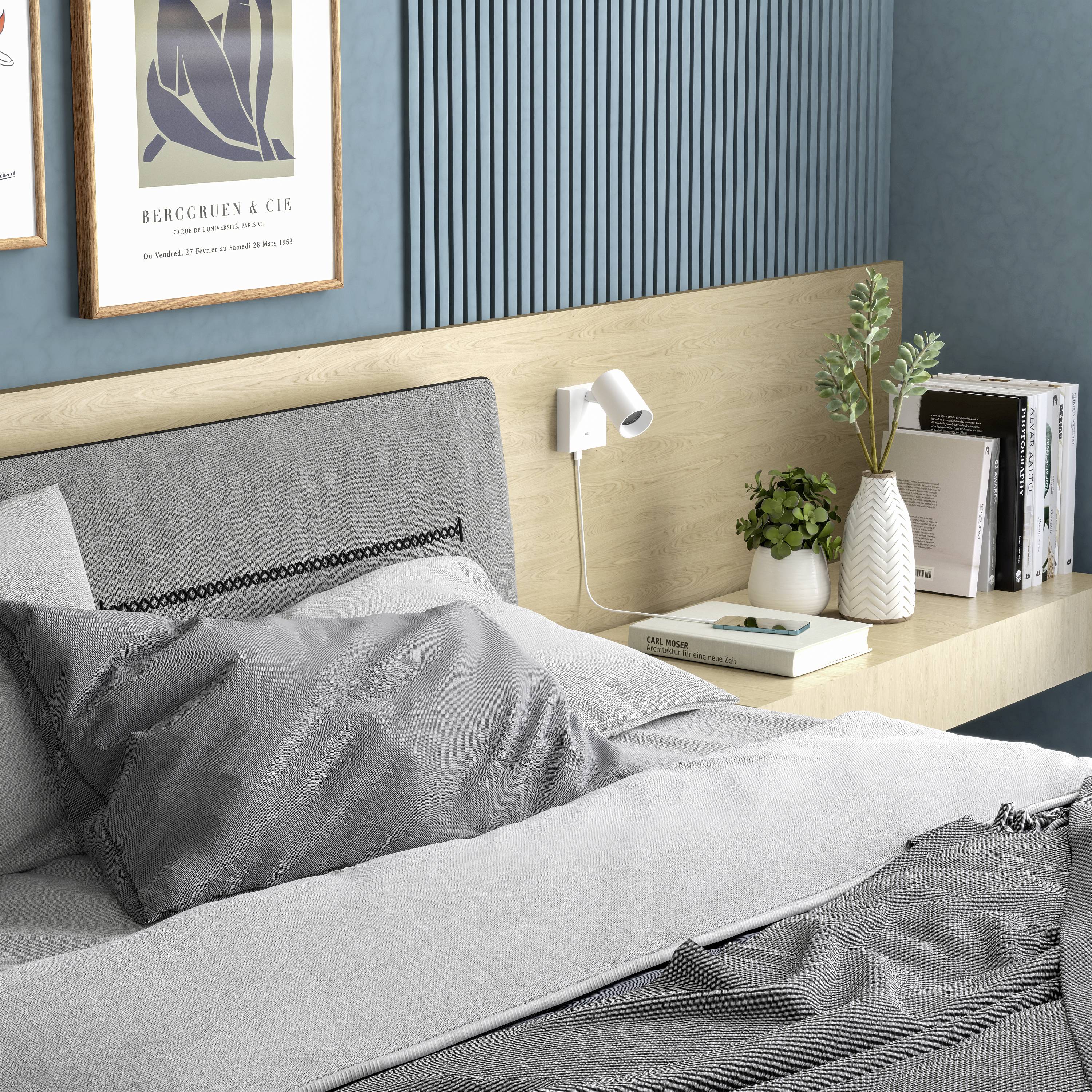 Ein modern eingerichtetes Schlafzimmer mit Holzwandregal, dekorativen Pflanzen und Büchern. Ein graues Kopfkissen liegt auf dem Bett.