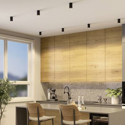 Moderne Küche mit Holzelementen, zwei Barhockern und einem Fenster. Helle Beleuchtung und grüne Pflanze auf der Arbeitsplatte.