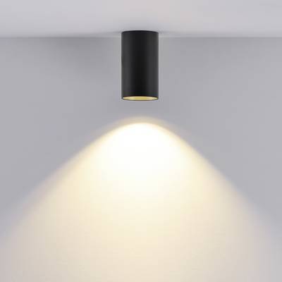 Schwarze Deckenlampe strahlt warmes Licht auf weiße Wand. Minimalistisches Design, Betonung auf Beleuchtungseffekt.