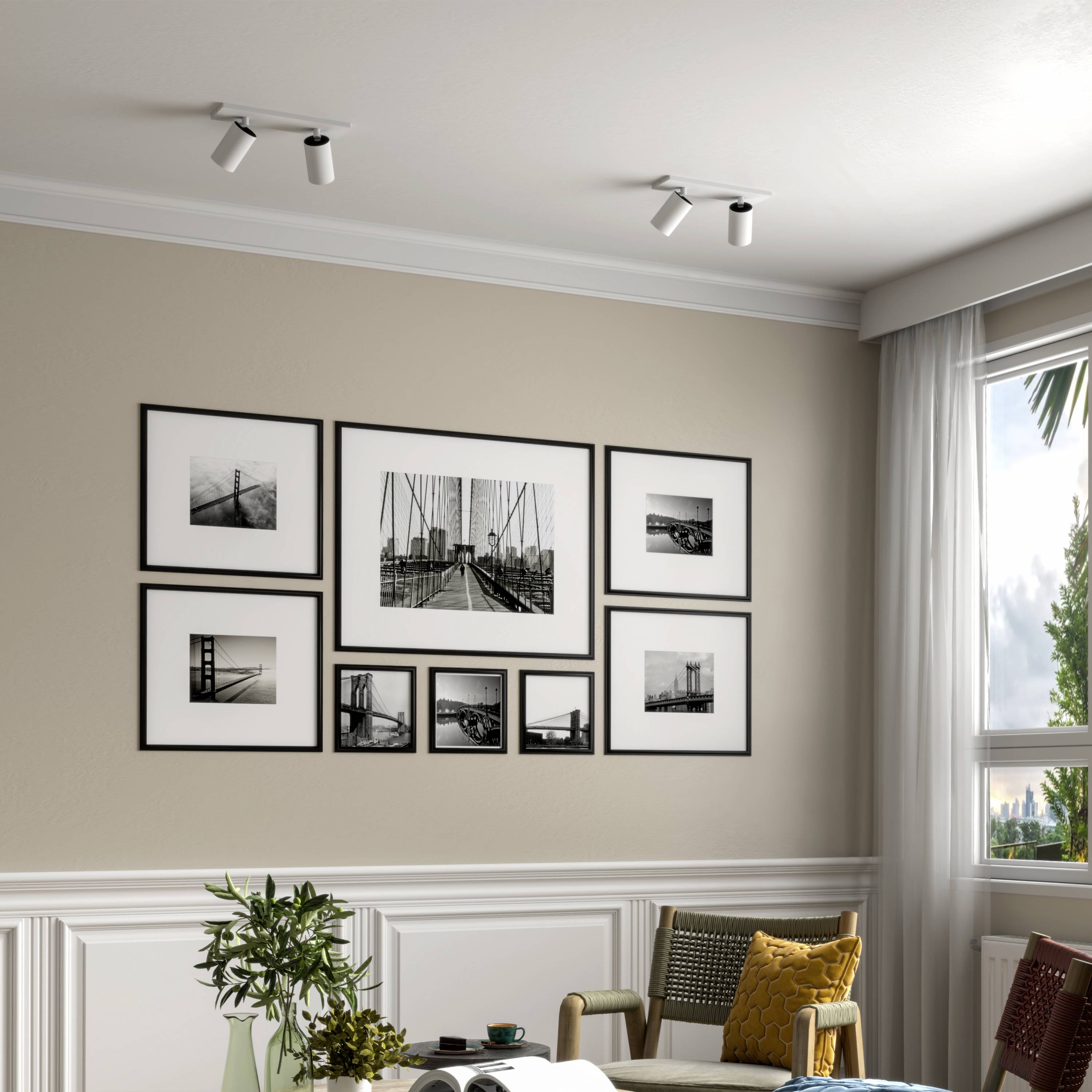 An einer beige gestrichenen Wand hängt eine Galerie aus schwarz-weißen Fotos mit Architekturmotiven. Darunter ein Tisch mit Dekorationen.