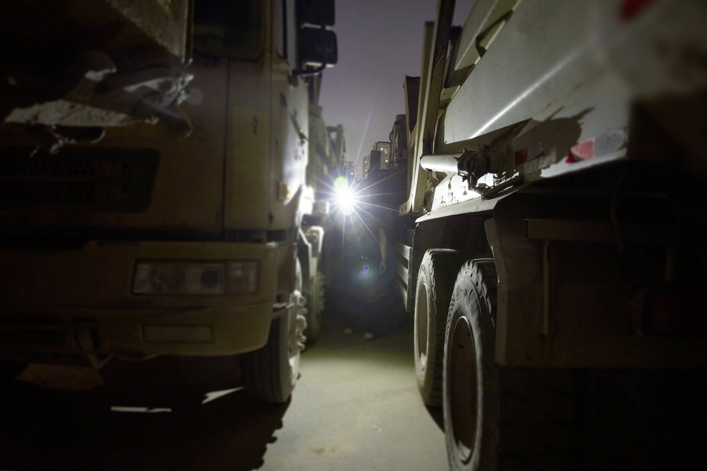Ein heller Lichtstrahl scheint in der Dunkelheit zwischen zwei eng geparkten Lastwagen, beleuchtet den schmalen Durchgang.
