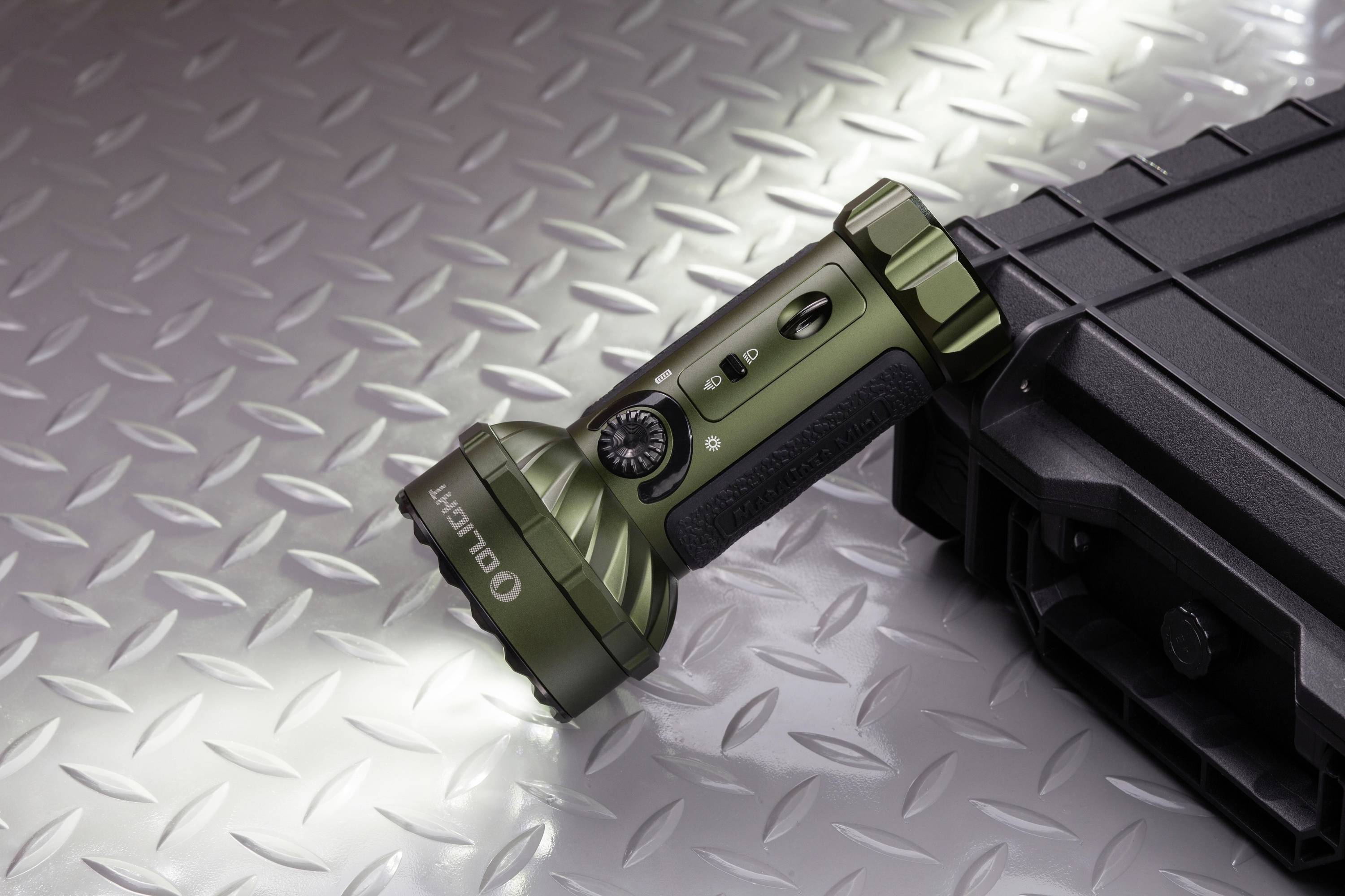 Eine grüne Taschenlampe liegt auf einem schwarzen Koffer auf einer metallischen Oberfläche. Die Taschenlampe zeigt nach links.