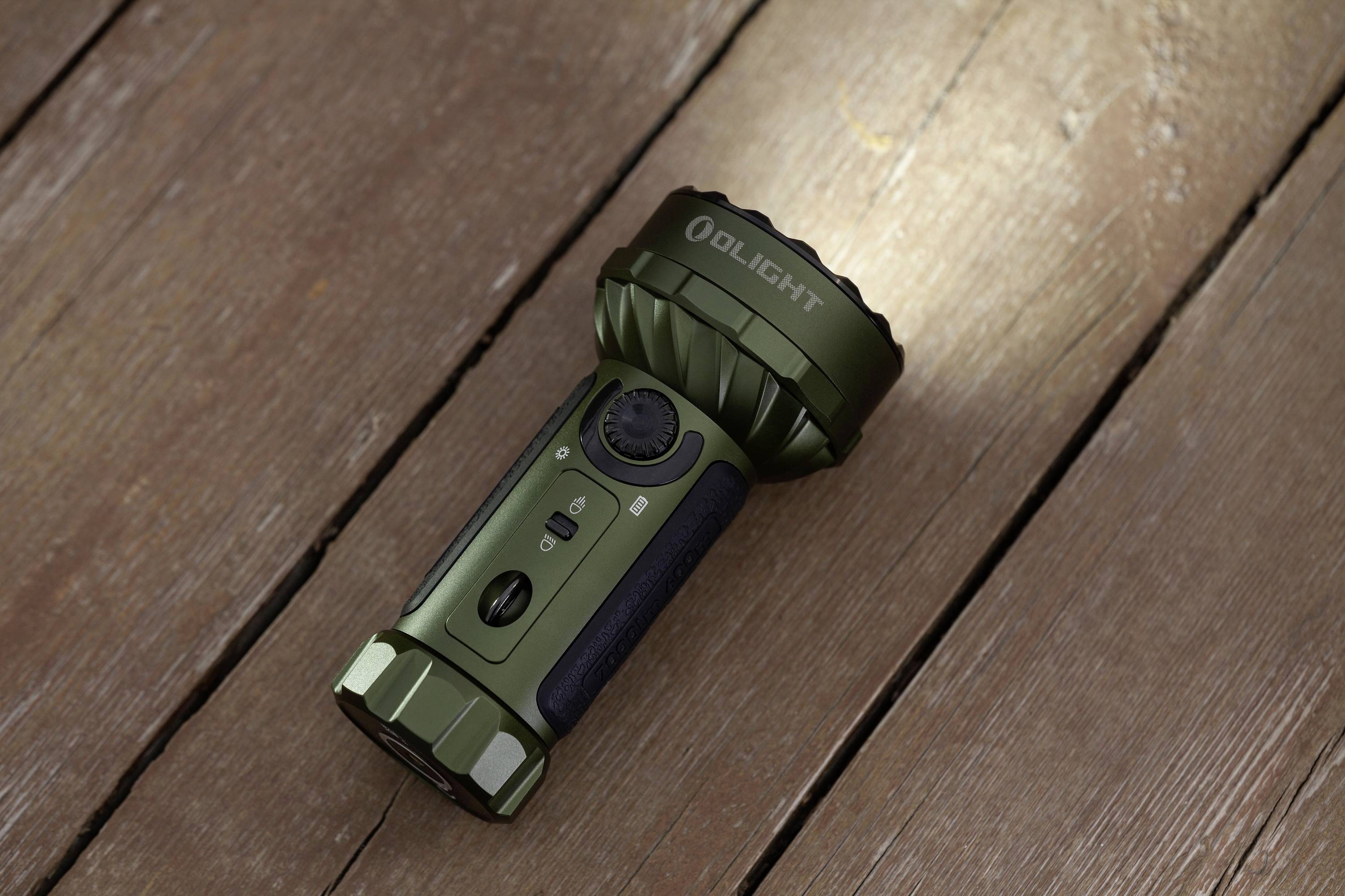 Grüne Taschenlampe liegt auf einem Holzboden. Sie ist eingeschaltet und strahlt Licht auf den Boden.