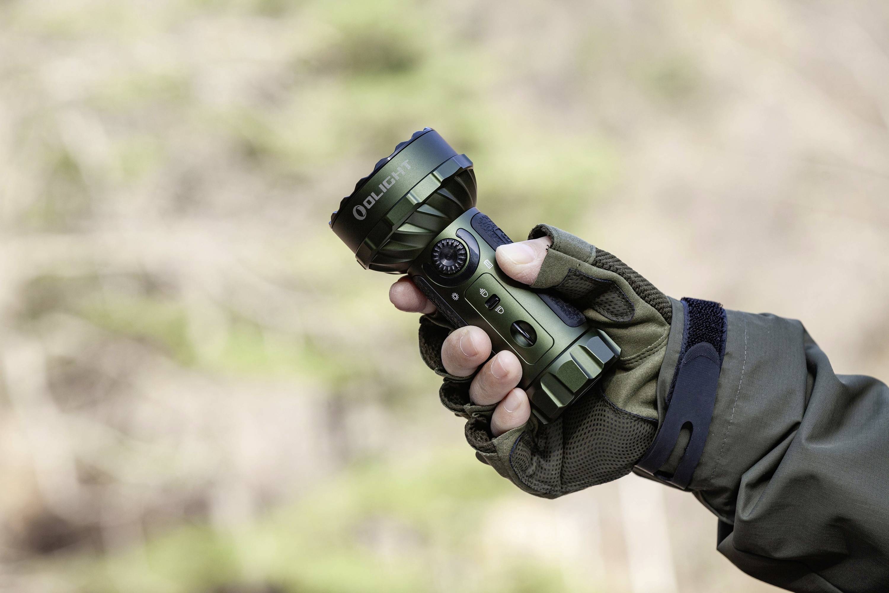 Eine Hand hält eine kompakte, grüne Taschenlampe mit mehreren Funktionen. Die Person trägt einen Handschuh und eine Outdoor-Jacke.