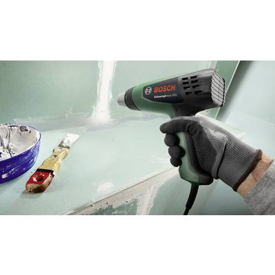 'Ein Handschuh hält ein Bosch-Heißluftgebläse nahe einer Wand, wo eine Spachtel und Farbe auf einer Palette sichtbar sind.'