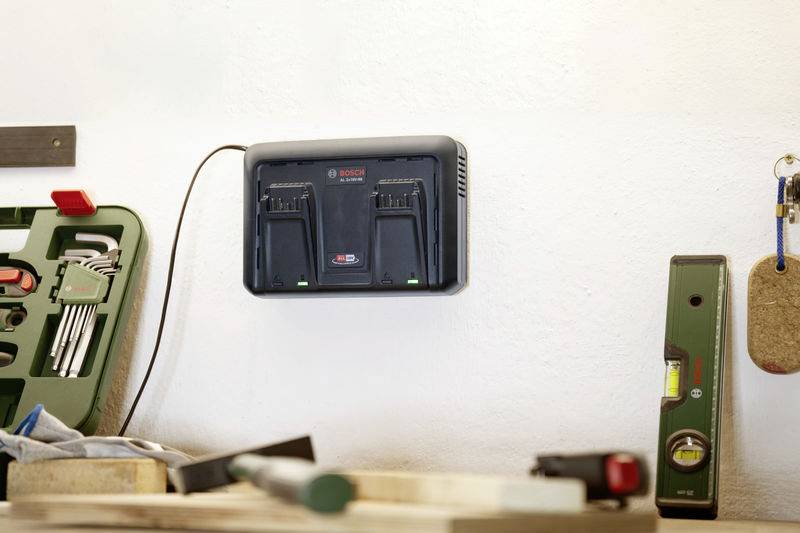 Eine Werkstattwand mit einem montierten Ladegerät für Akkus. Daneben stehen eine Kiste mit Werkzeugen und eine Wasserwaage.