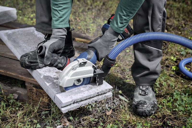 Eine Person schneidet mit einer elektrischen Säge ein Betonbrett. Schutzkleidung, einschließlich Handschuhen und Stiefeln, wird getragen.