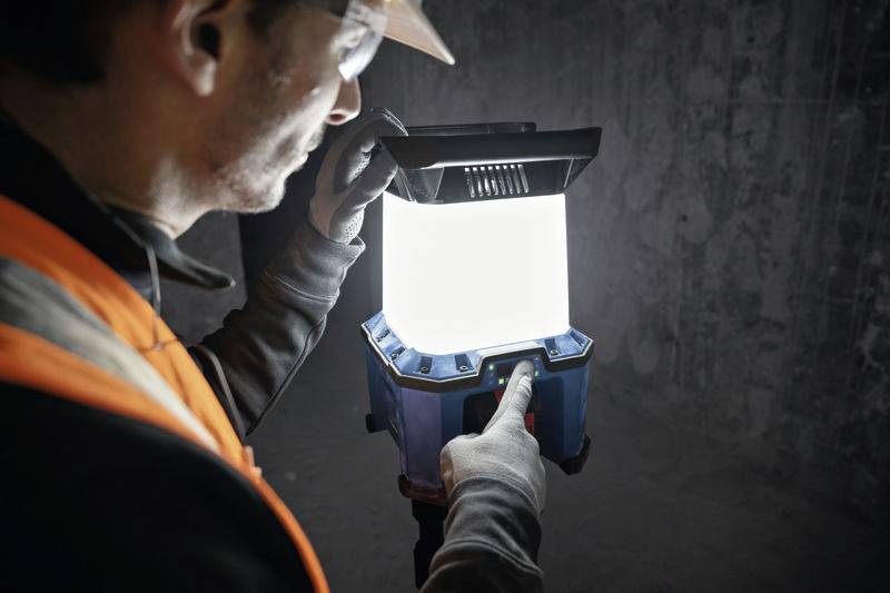 Eine Person in Sicherheitskleidung drückt einen Knopf auf einer hell leuchtenden, tragbaren Laterne in einem dunklen Raum.