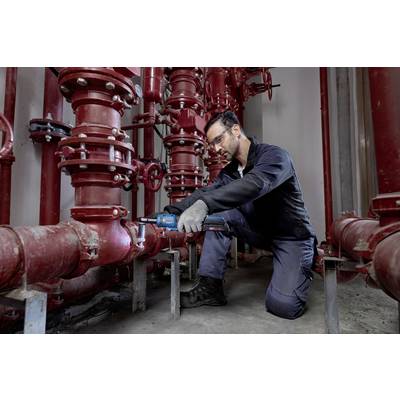 Ein Techniker repariert ein rotes Rohrleitungssystem in einem Industriegebäude. Er trägt Schutzbrille und Arbeitshandschuhe.