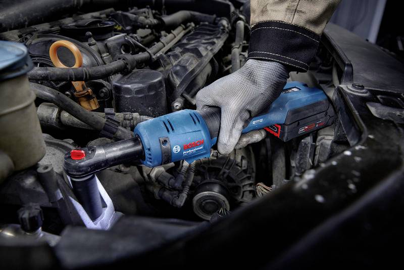 Eine Person repariert einen Auto-Motor mit einem blauen Bosch-Akkuschrauber. Der Motorraum ist detailliert sichtbar.