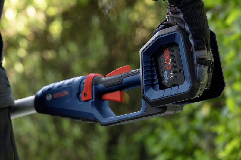 Nahaufnahme eines Bosch-Gartengeräts mit einem ProCORE Akku, gehalten von einer Person mit Handschuhen. Im Hintergrund sind Bäume sichtbar.