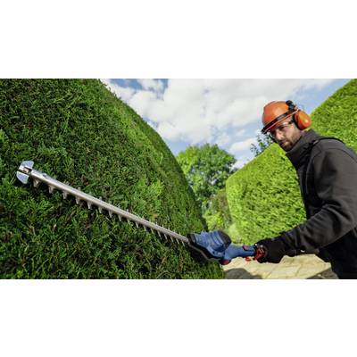 Ein Mann mit Schutzhelm und Gehörschutz schneidet eine Hecke mit einer elektrischen Heckenschere, umgeben von grünen Büschen.