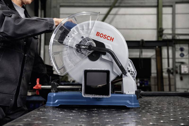 'Person bedient eine Bosch-Metallsäge auf einem Tisch in einer Werkstattumgebung.'