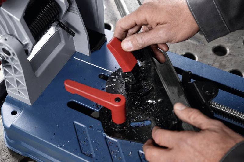 Zwei Hände bedienen eine Metallsäge, Justierung der Winkeleinstellung mit roten Hebeln.