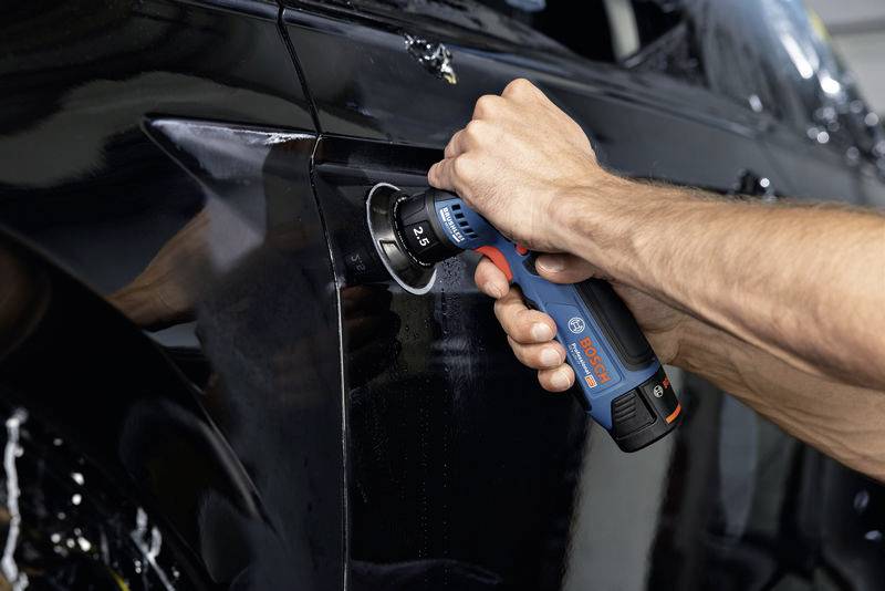 Eine Person benutzt einen Akkuschrauber, um eine Schraube in der Karosserie eines schwarzen Autos anzuziehen.