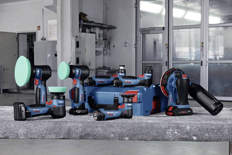 Diverse Elektrowerkzeuge und Zubehör auf grauem Tisch in Werkstatt, darunter Bohrer, Polierer und Akkuladegerät.