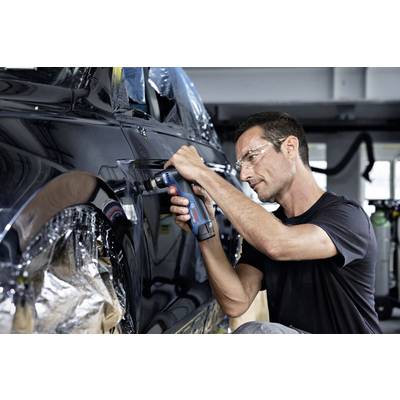 Ein Mann in Schutzbrille arbeitet mit einem Bohrwerkzeug an einem schwarzen Auto in einer Werkstatt.