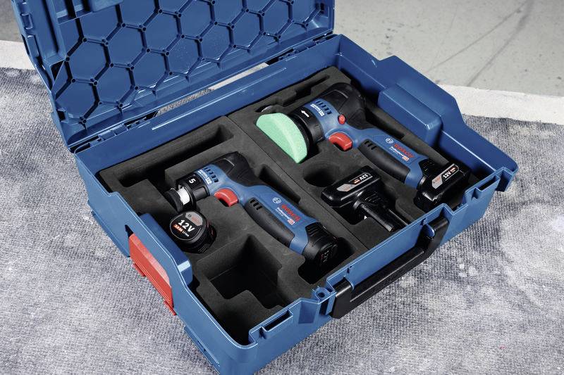 Ein blauer Werkzeugkoffer enthält zwei blaue Akkuschrauber mit rotem Detail, zwei Akkus und ein Ladegerät, auf grauem Boden liegend.